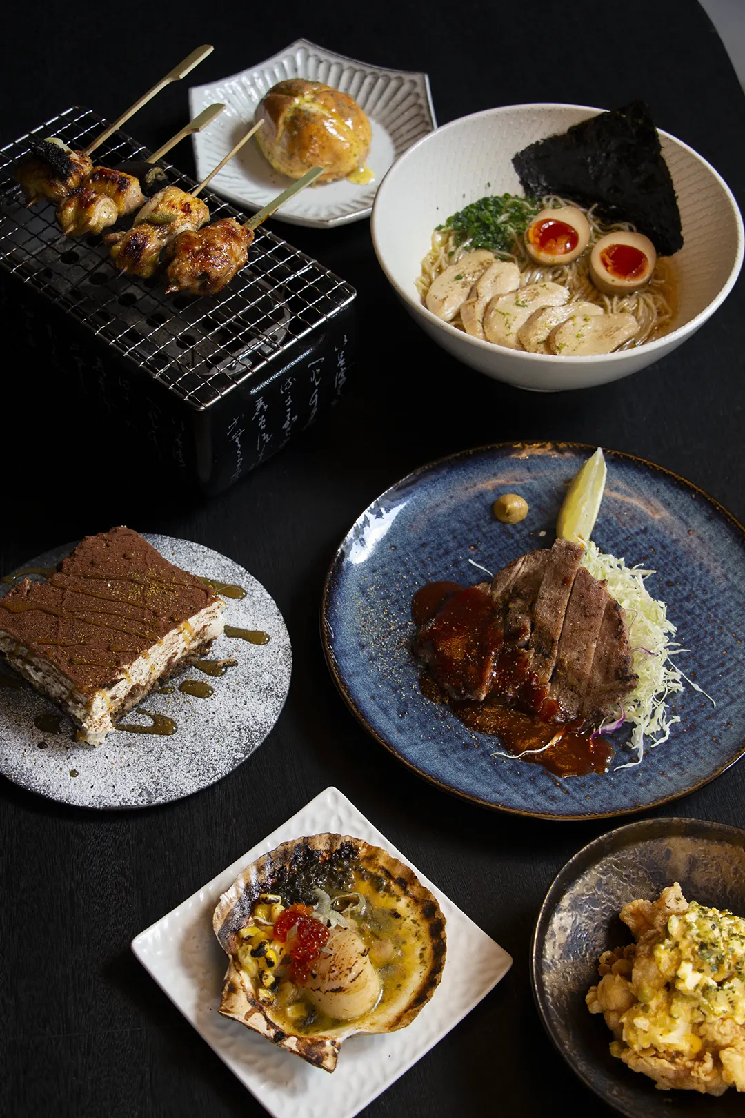 A selection of Japanese dishes from Shin Terroir, including garlic butter bun, signature chicken ramen, our tiramiso and seafood appetizers served in artisanal ceramic bowls.