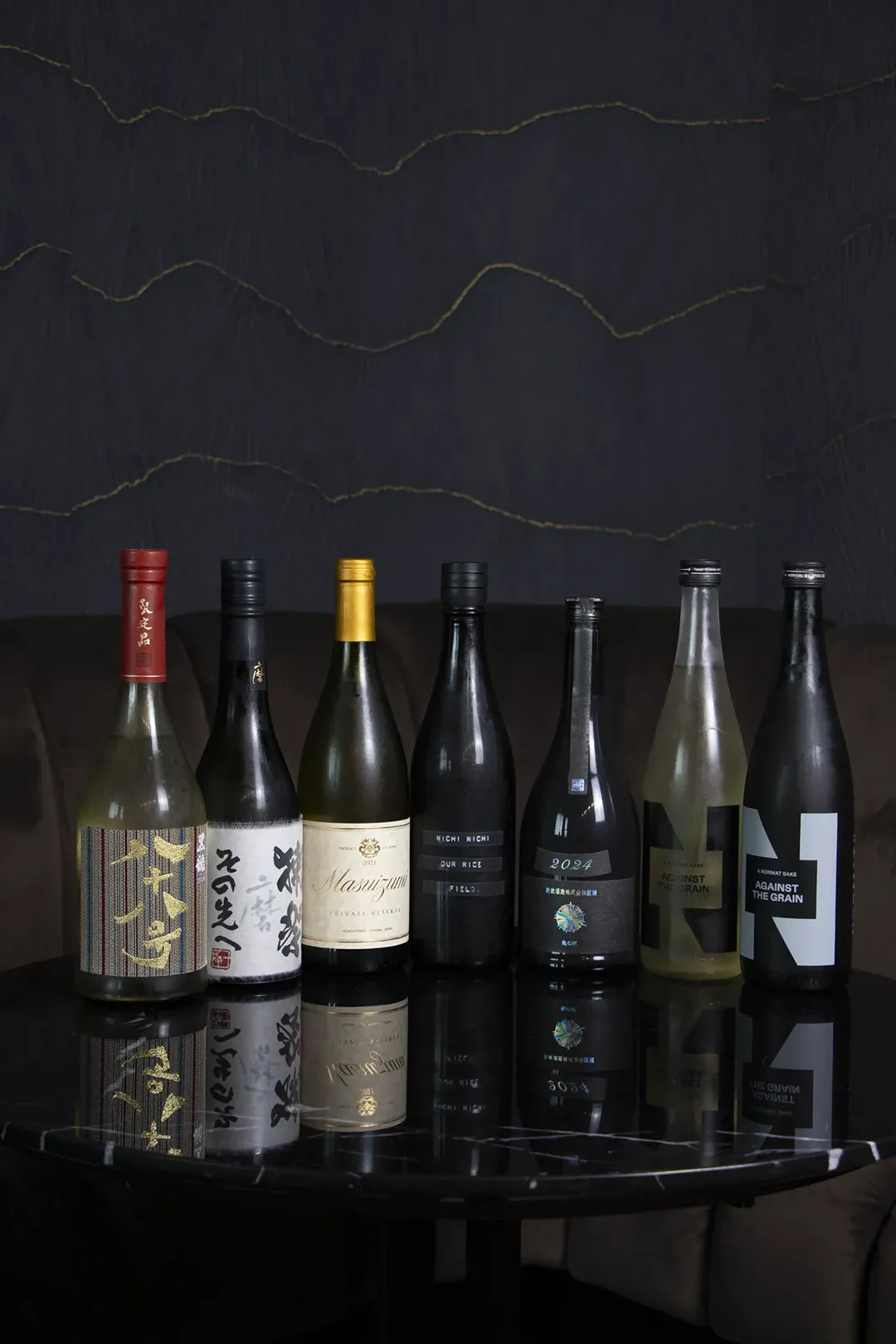 Eight bottles of Japanese sake from the Shin Terroir list, arranged on a dark table.